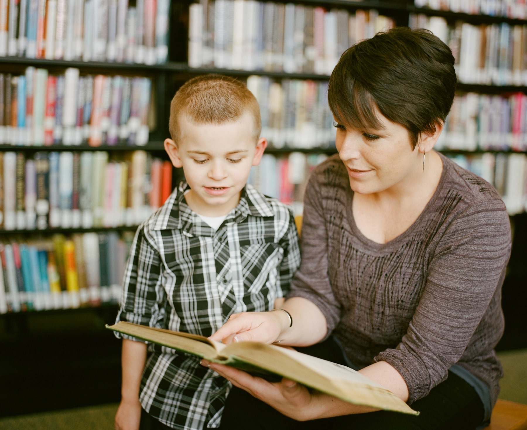 A teacher and a boy reading a book together
